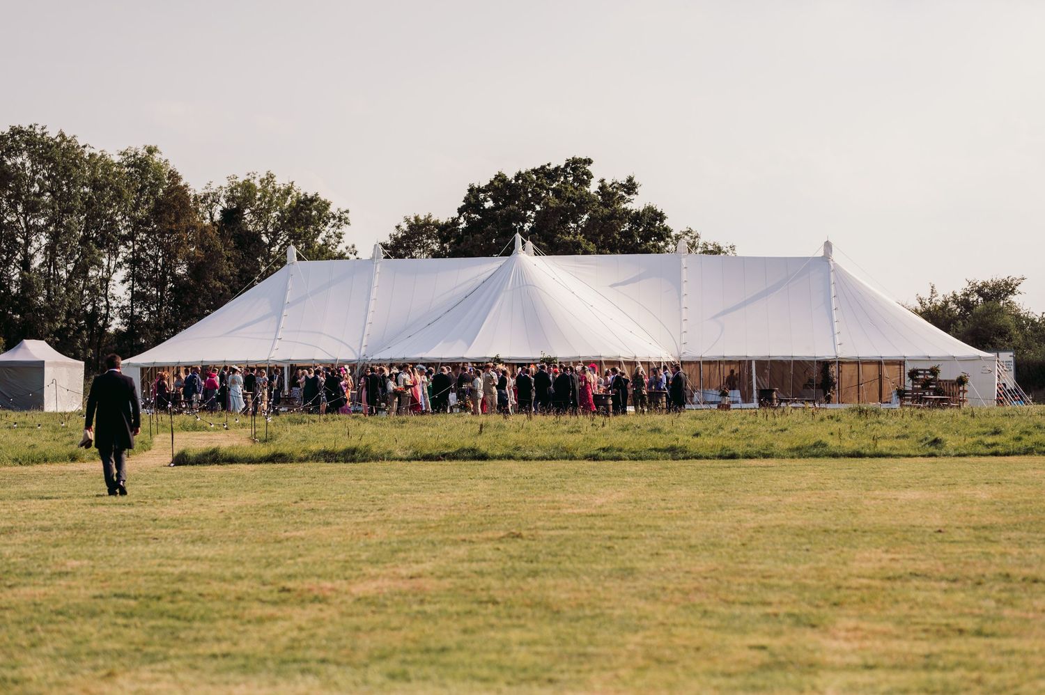Large white wedding tent set up in a grassy field on a sunny day.