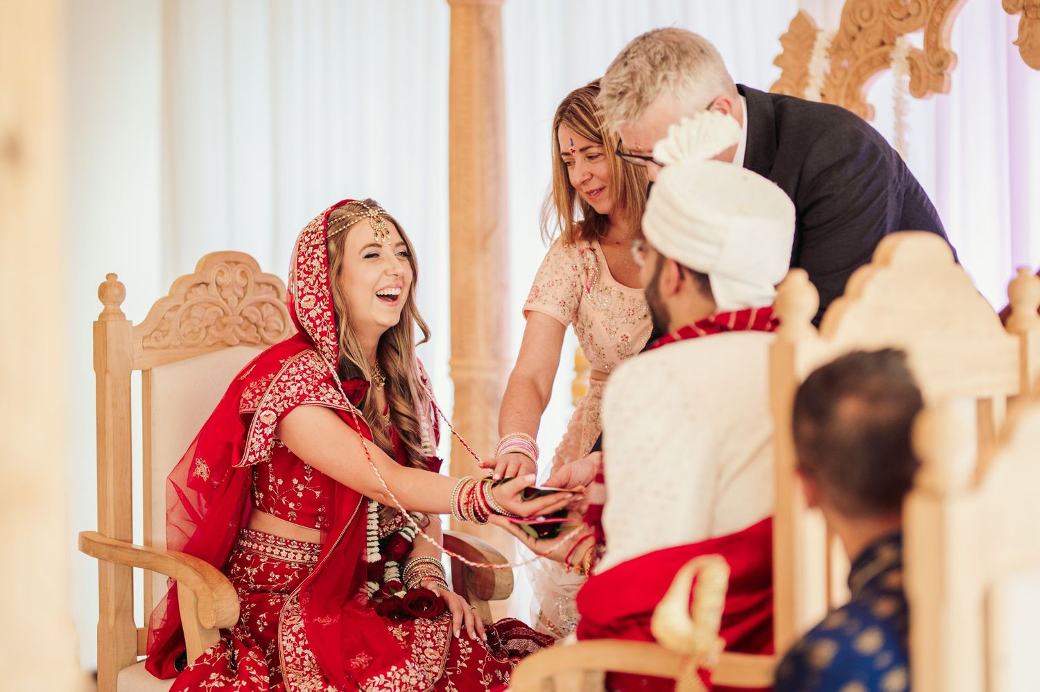 A joyful moment captured during an Indian wedding ceremony with participants in traditional red and white attire.