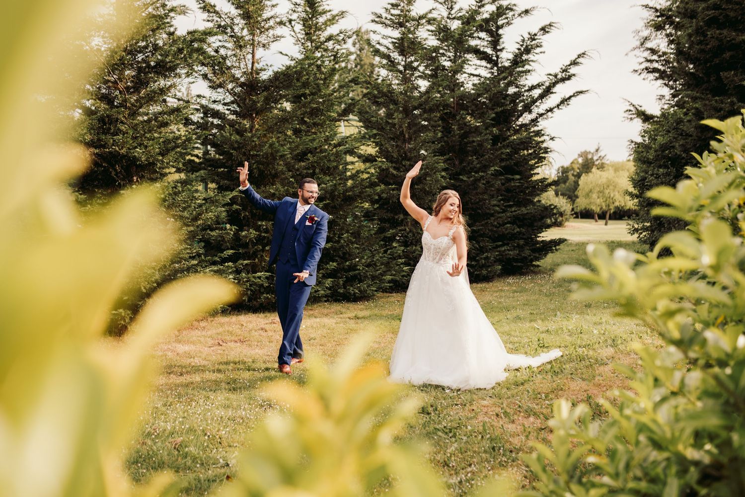 A joyful couple dances outdoors on their wedding day surrounded by evergreen trees and natural foliage.