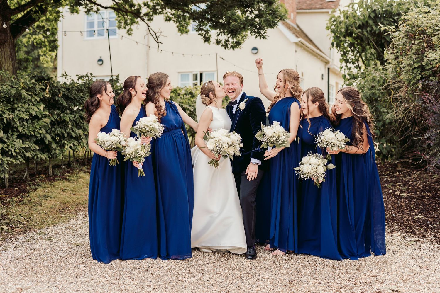 Wedding party poses together outdoors in coordinating royal blue dresses and light floral bouquets.
