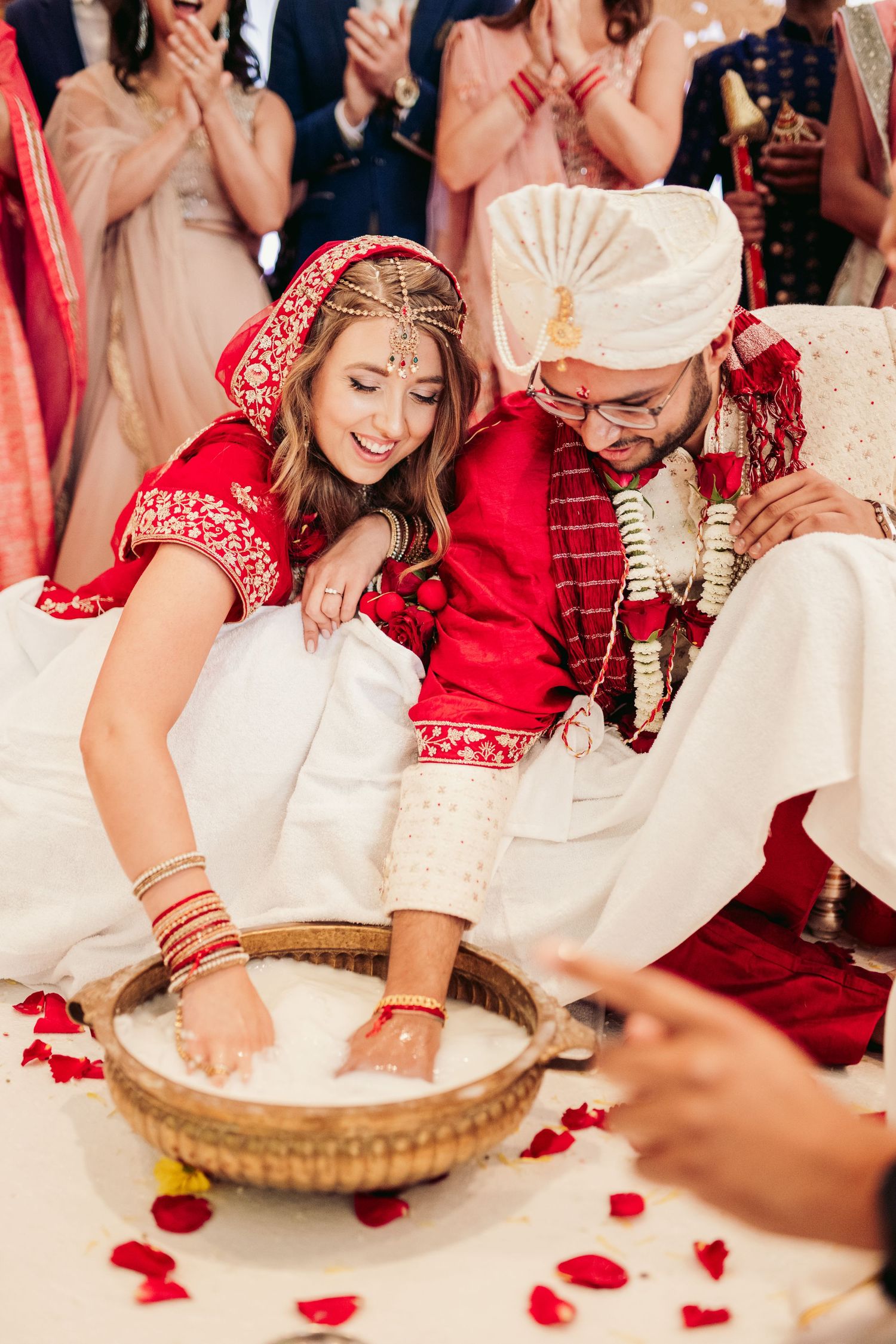 A couple participates in a traditional Hindu wedding ceremony ritual with a rice-filled basket surrounded by rose petals.
