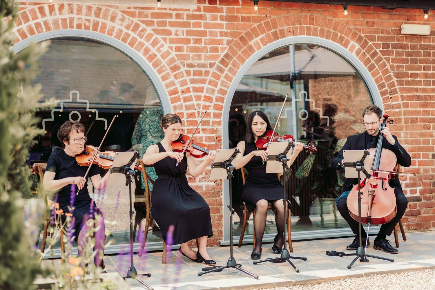 String quartet performs classical music in front of a brick archway during an outdoor event.