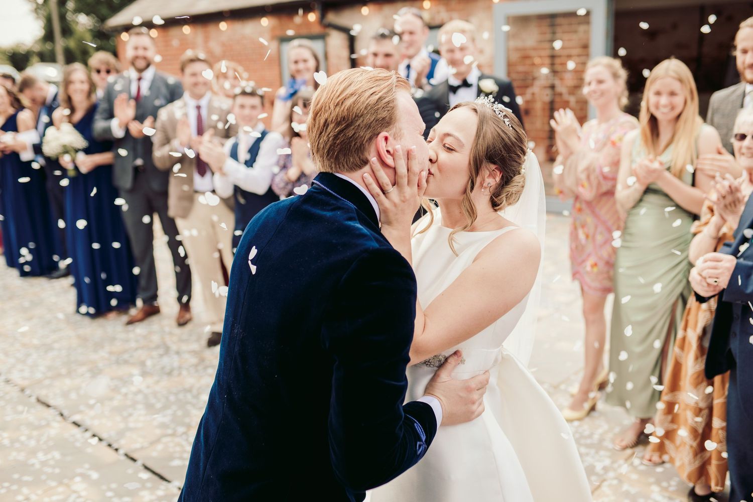A couple shares a romantic kiss during their wedding celebration as guests shower them with confetti and sparklers.