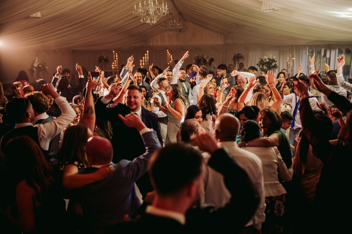 Energetic crowd with raised arms dancing at a lively wedding reception party.