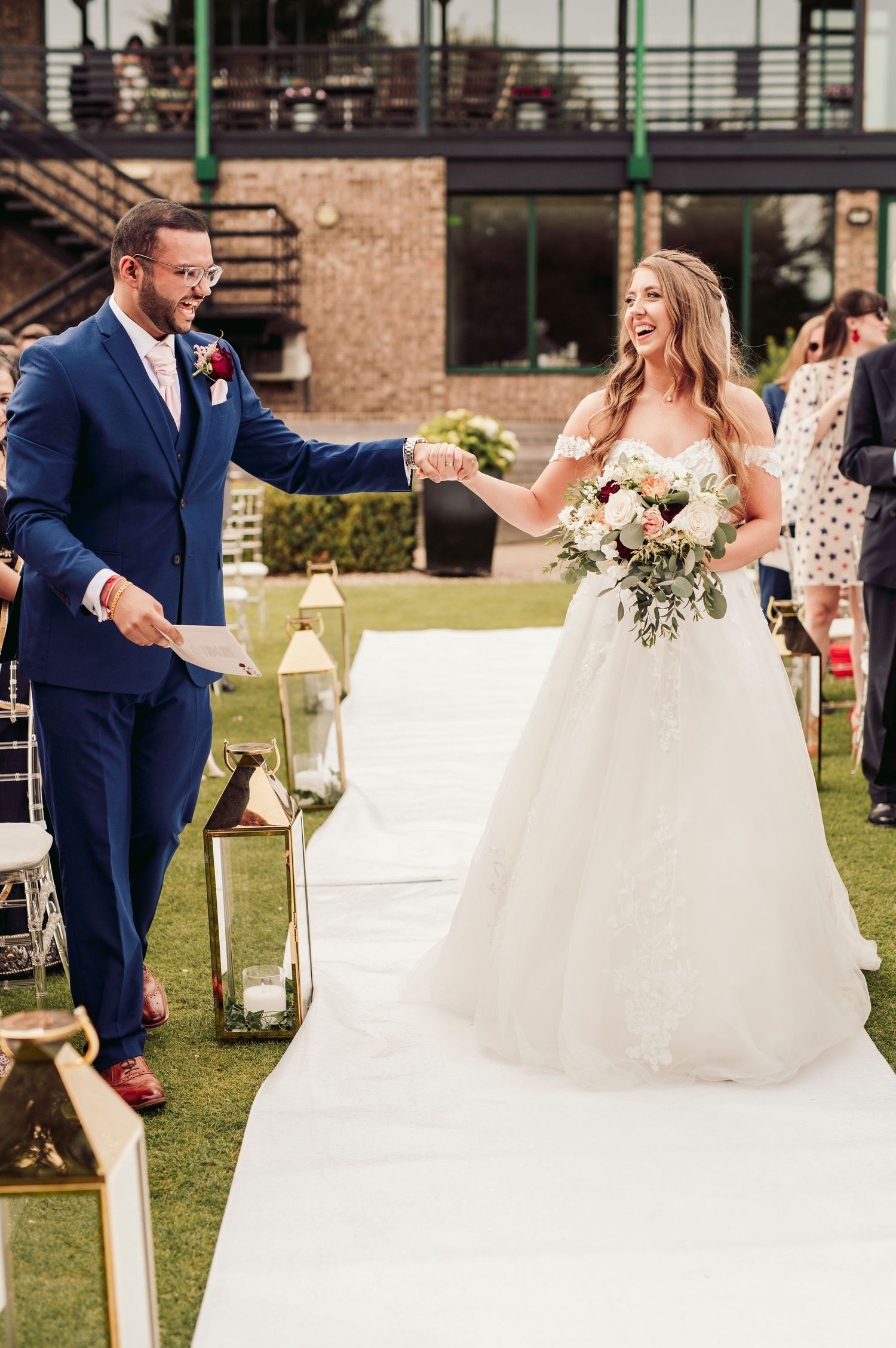 A couple shares a joyful moment during their outdoor wedding ceremony on a lush green lawn.