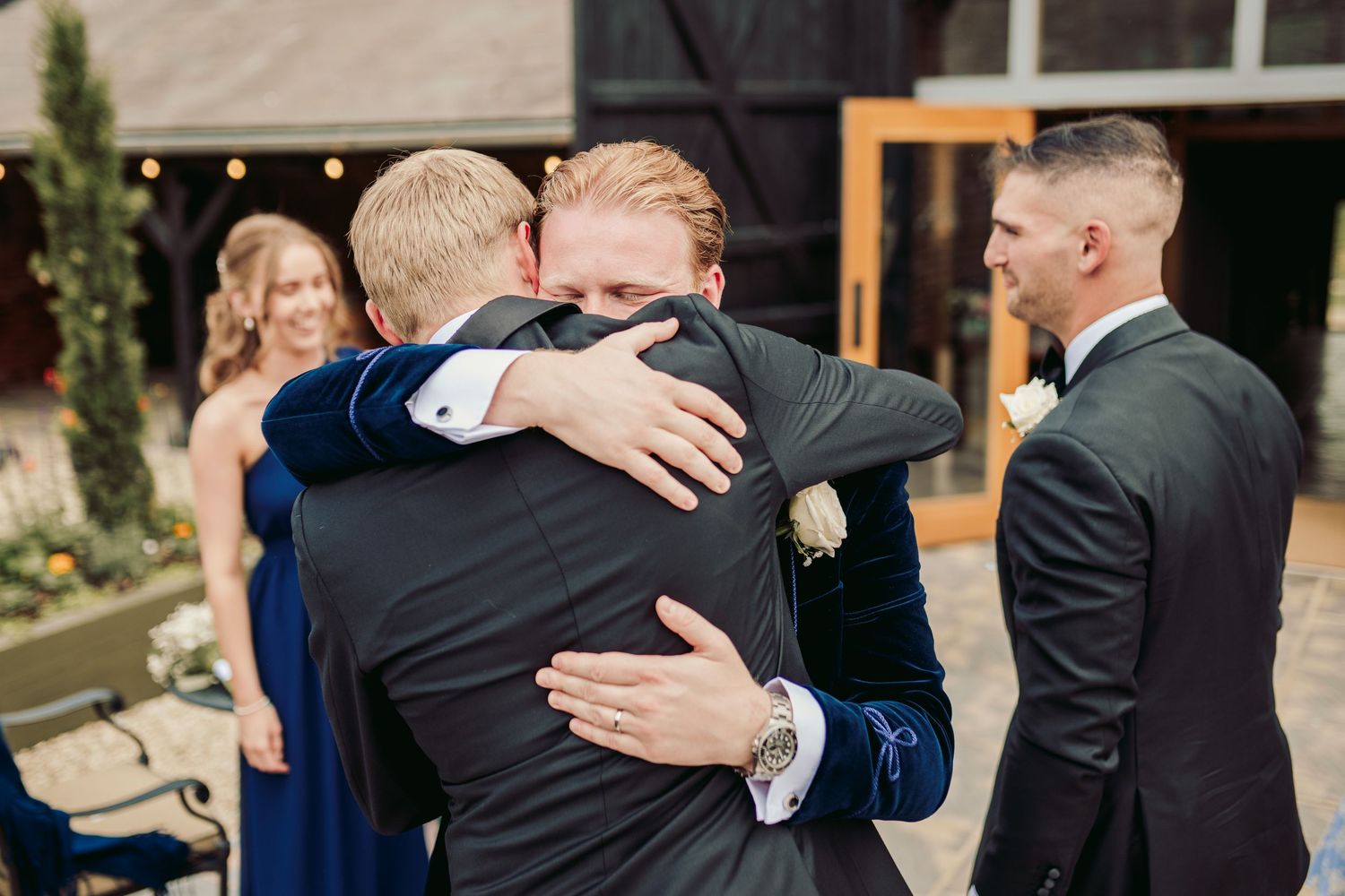 A series of emotional embraces between wedding guests in formal attire at an outdoor celebration.