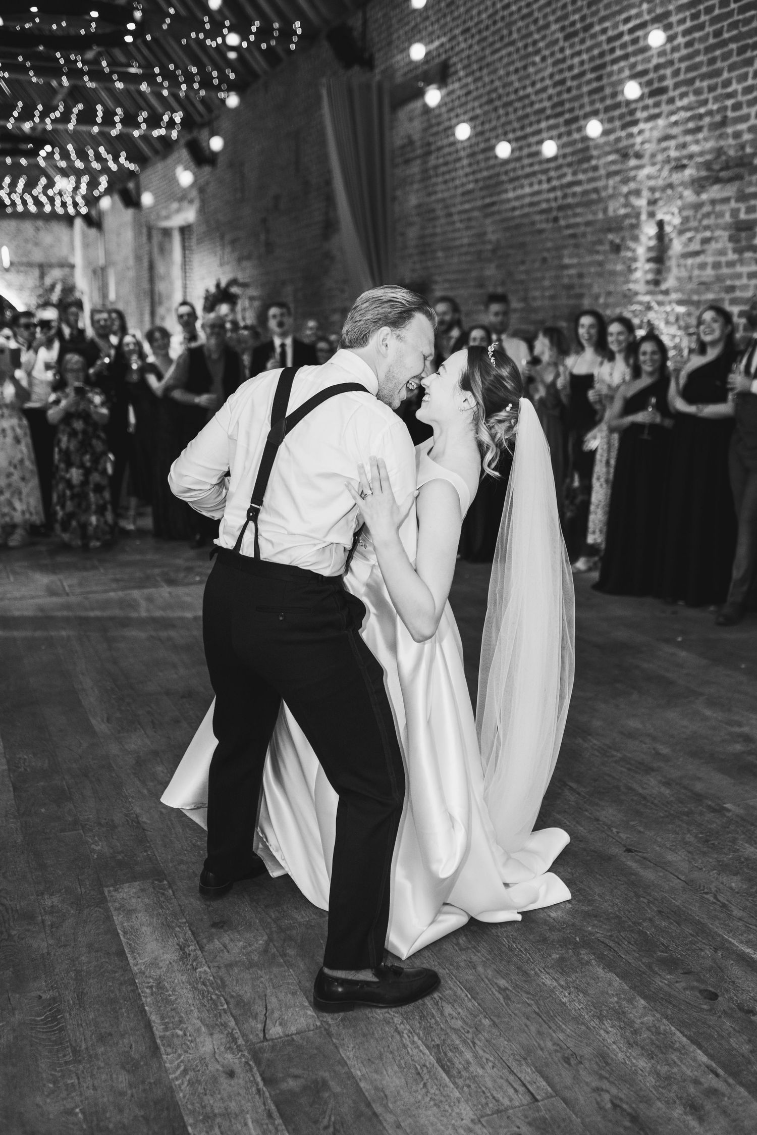 Wedding guests dance and twirl in white ghost costumes on a wooden dance floor under string lights at a reception.