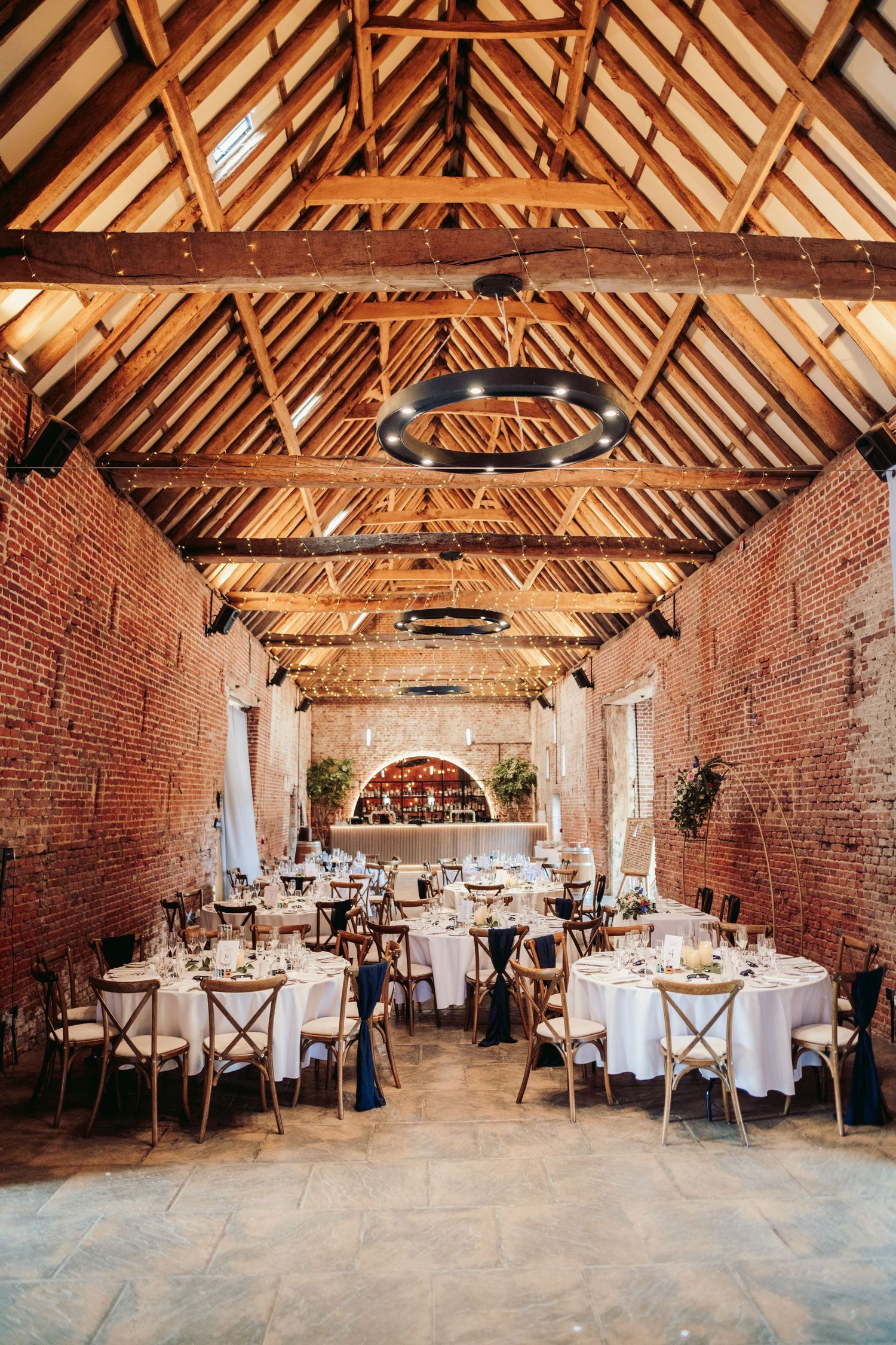 Rustic barn wedding venue with exposed brick walls, wooden beam ceiling, and elegant round tables set for reception.