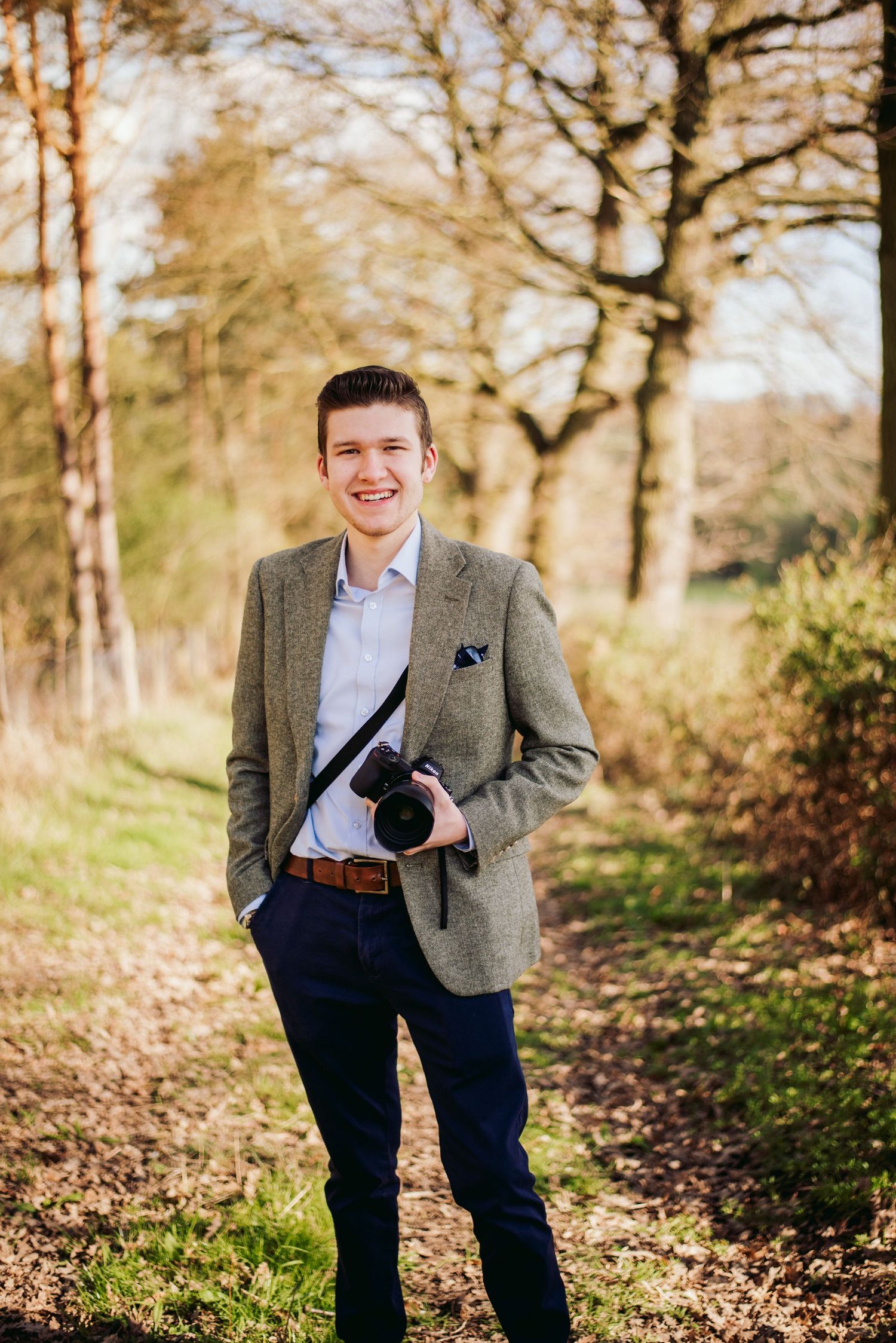 Portrait of photographer in casual business attire smiling on autumn forest path.