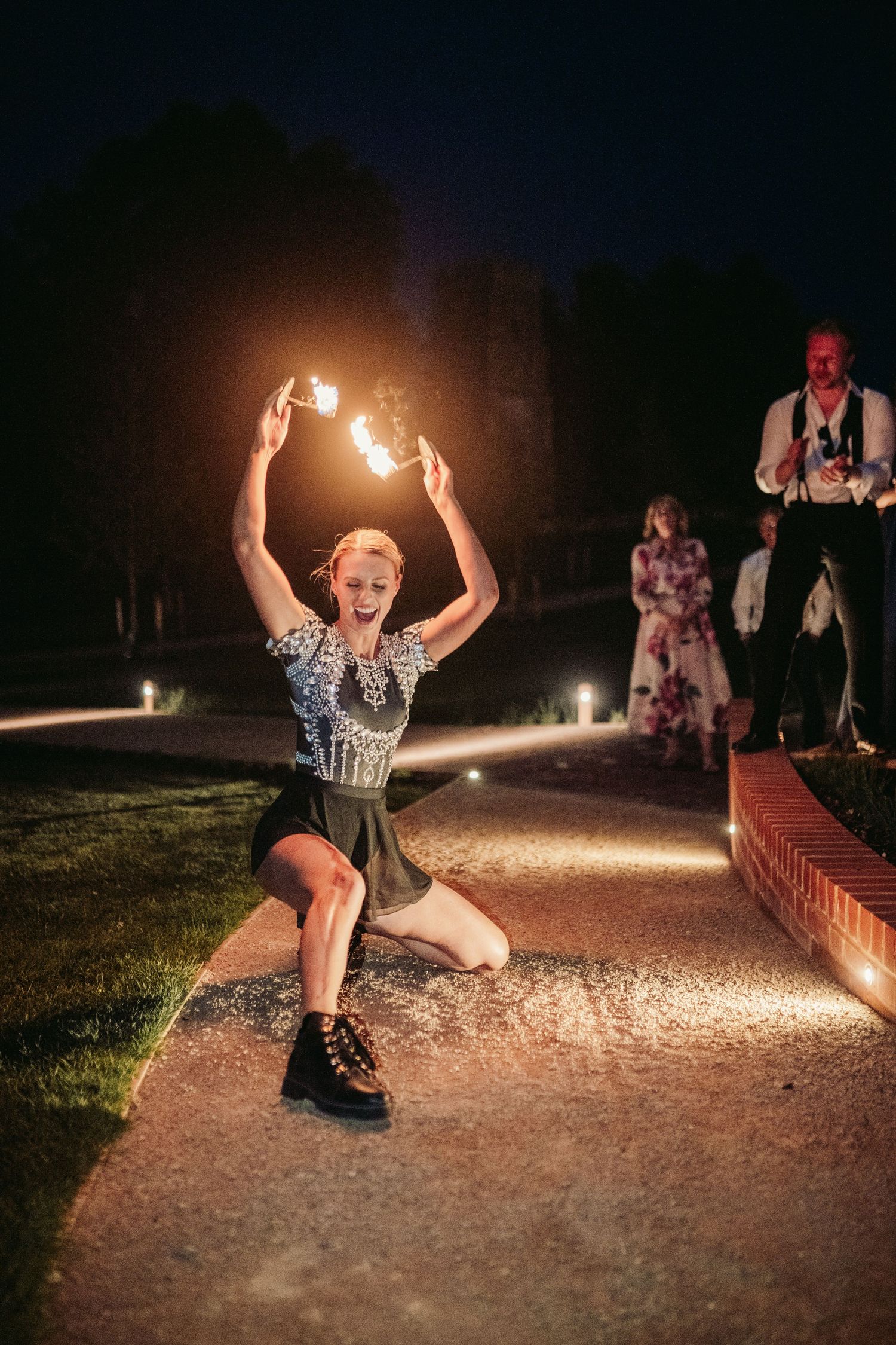 A person performs a dynamic jump split pose on a gravel path at night with dramatic lighting effects.