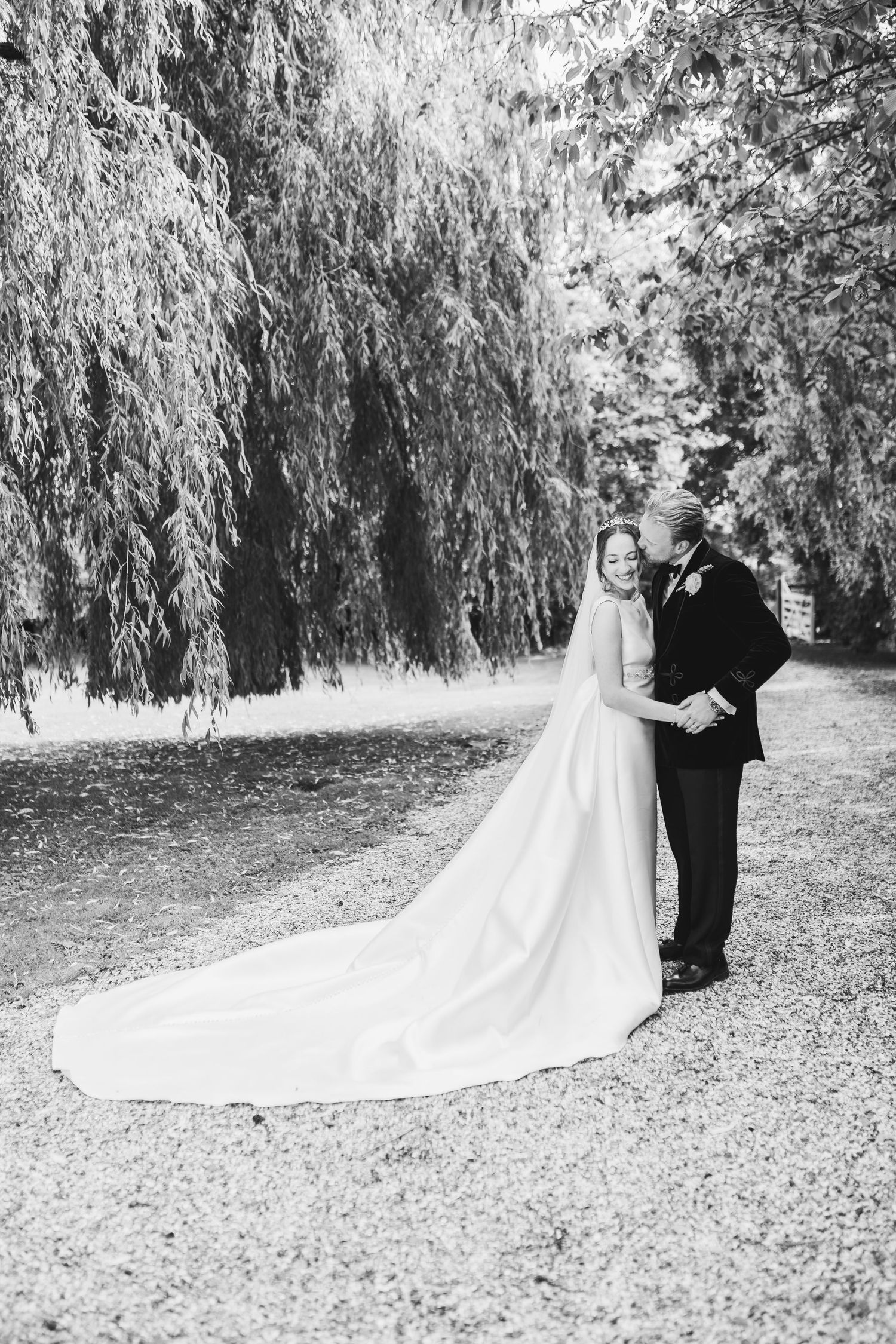 A romantic black and white photo series of a couple dancing under weeping willow trees in their wedding attire.
