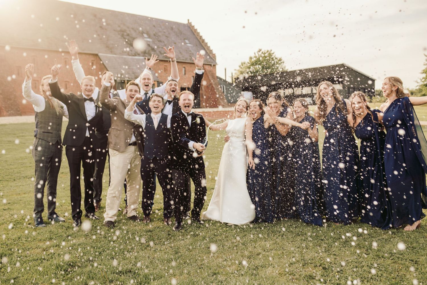Wedding guests celebrate with confetti and bubbles during an outdoor celebration on a sunny day.