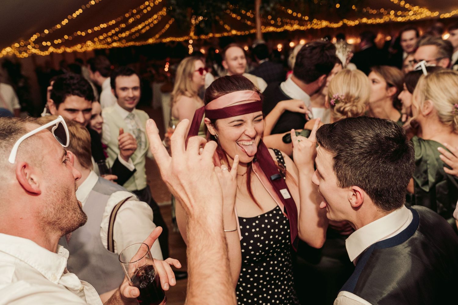 Lively dance party with string lights overhead at an evening wedding celebration.