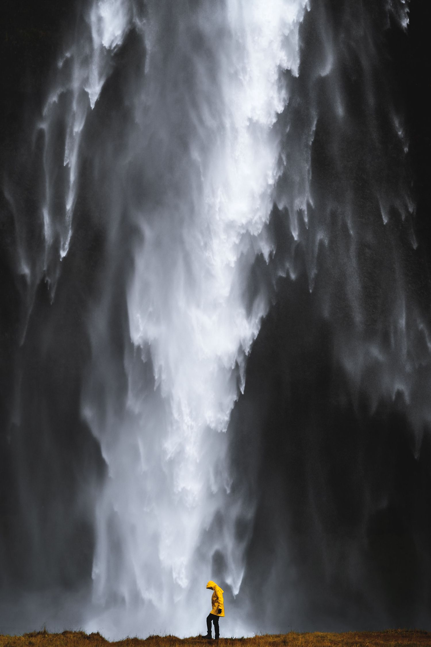 Seljalandsfoss Iceland, man in a yellow jacket stands at the base of the falls.