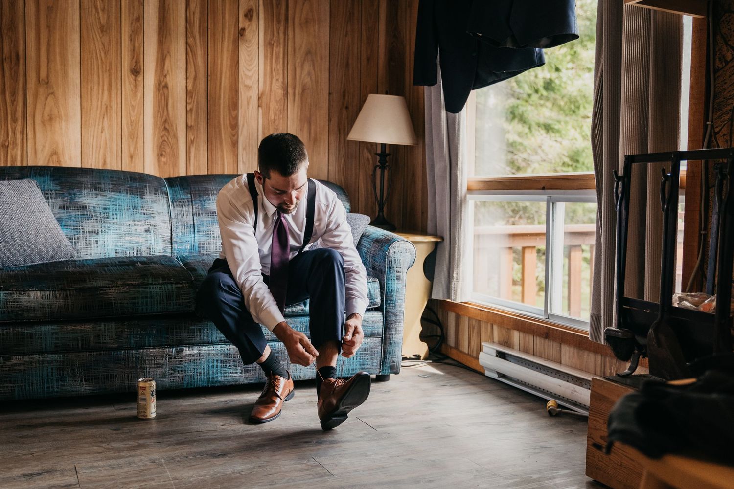 Groom ties his dress shoes inside a cottage while preparing for an intimate beachfront Muskoka wedding