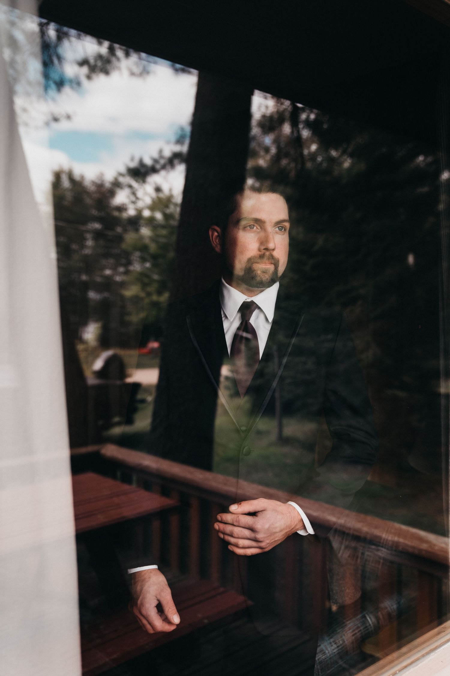 Groom staring longingly out of a cabin window while preparing for a beachfront wedding in Huntsville Ontario.