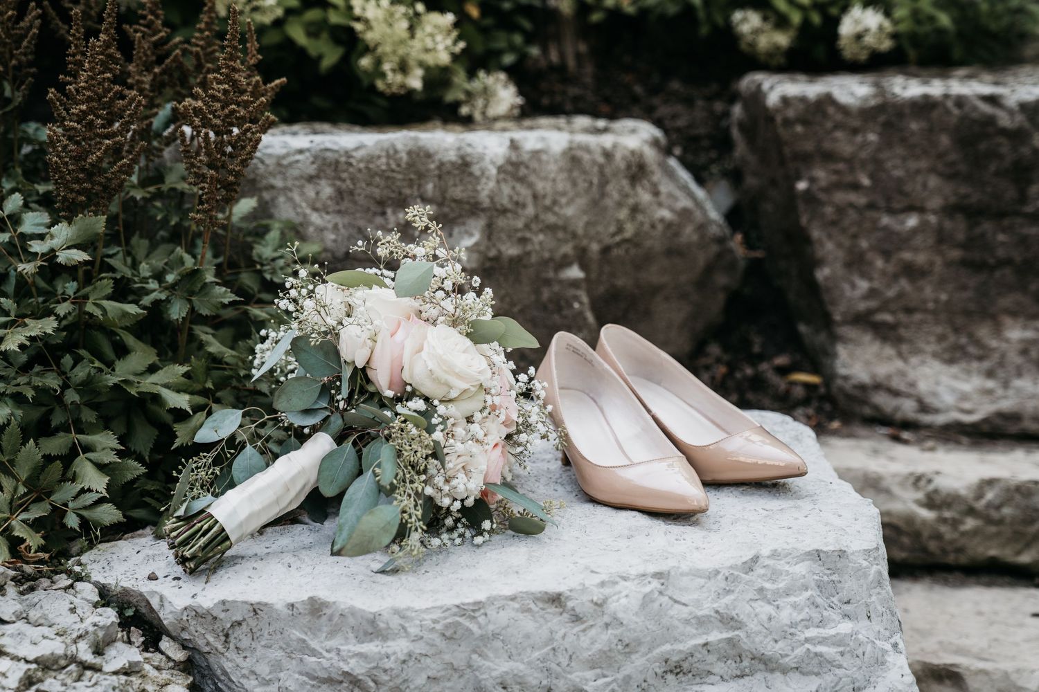 Bride's bouquet and shoes side by side on a decorative rock at the Old Mill, Toronto