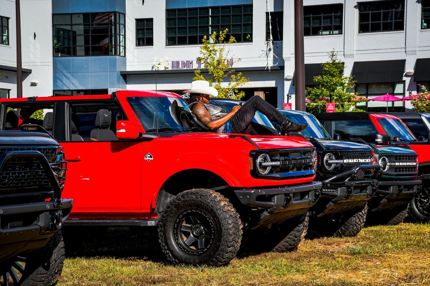 Red Ford Bronco with a person in a cowboy hat at an outdoor automotive show.
