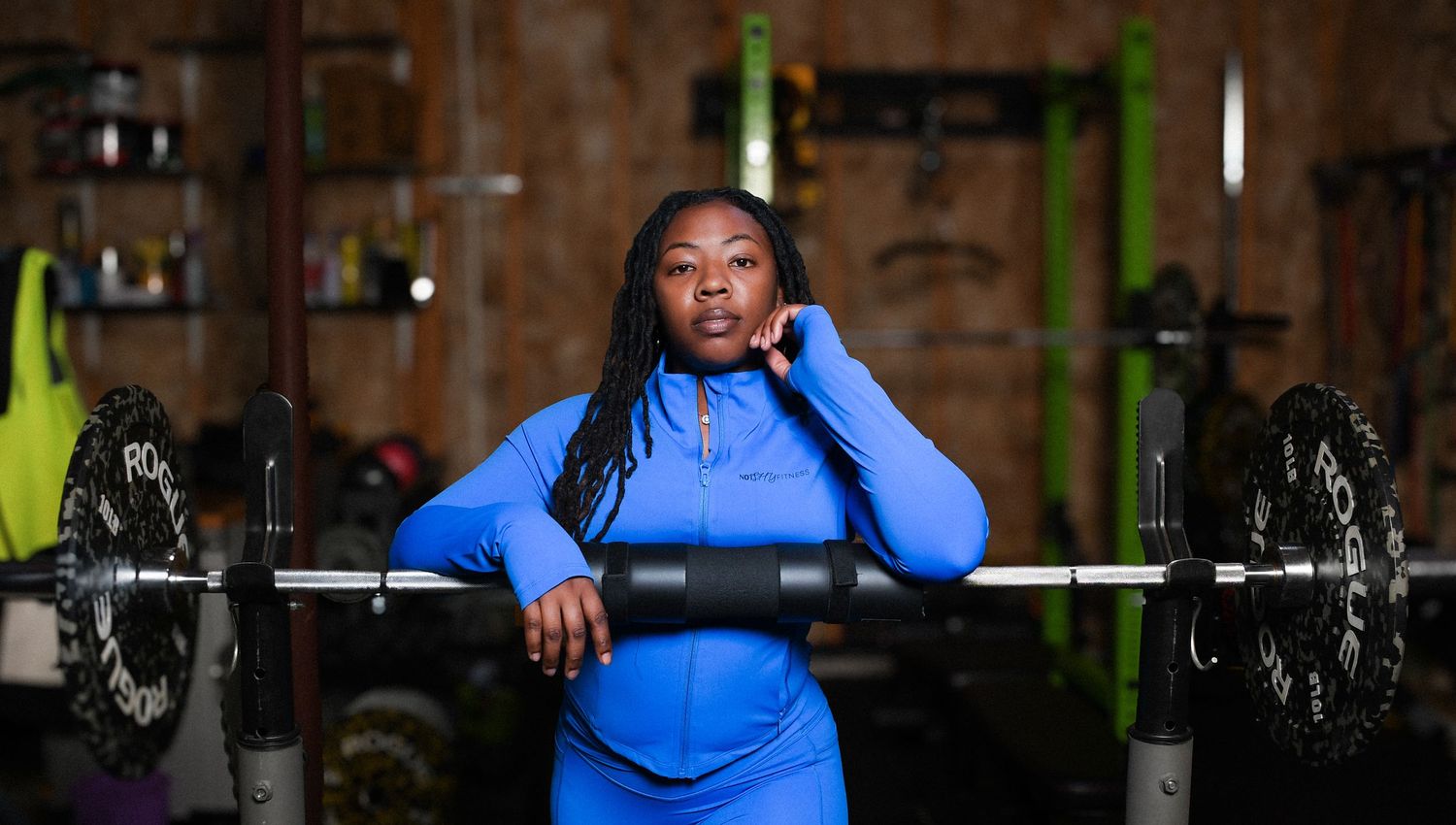Woman in blue athletic wear posing confidently in front of a barbell in a gym setting.