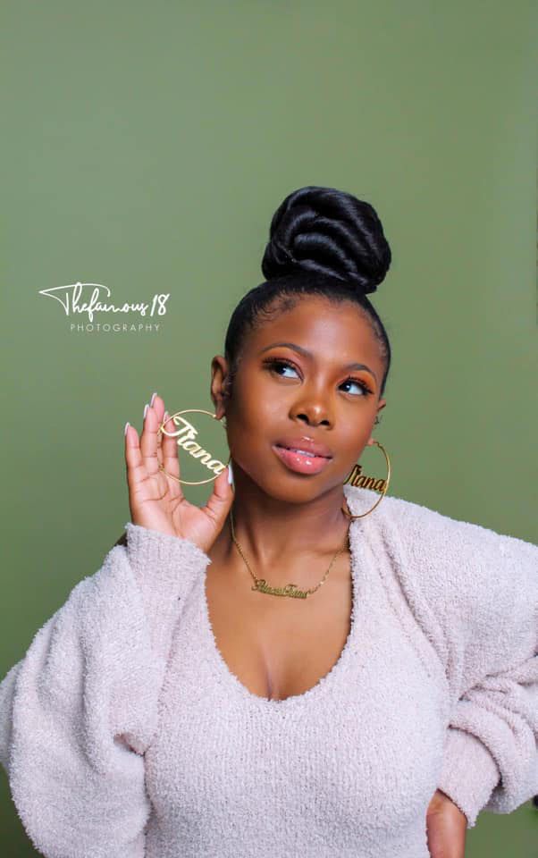 Young woman with bun updo in white sweater poses on green background.