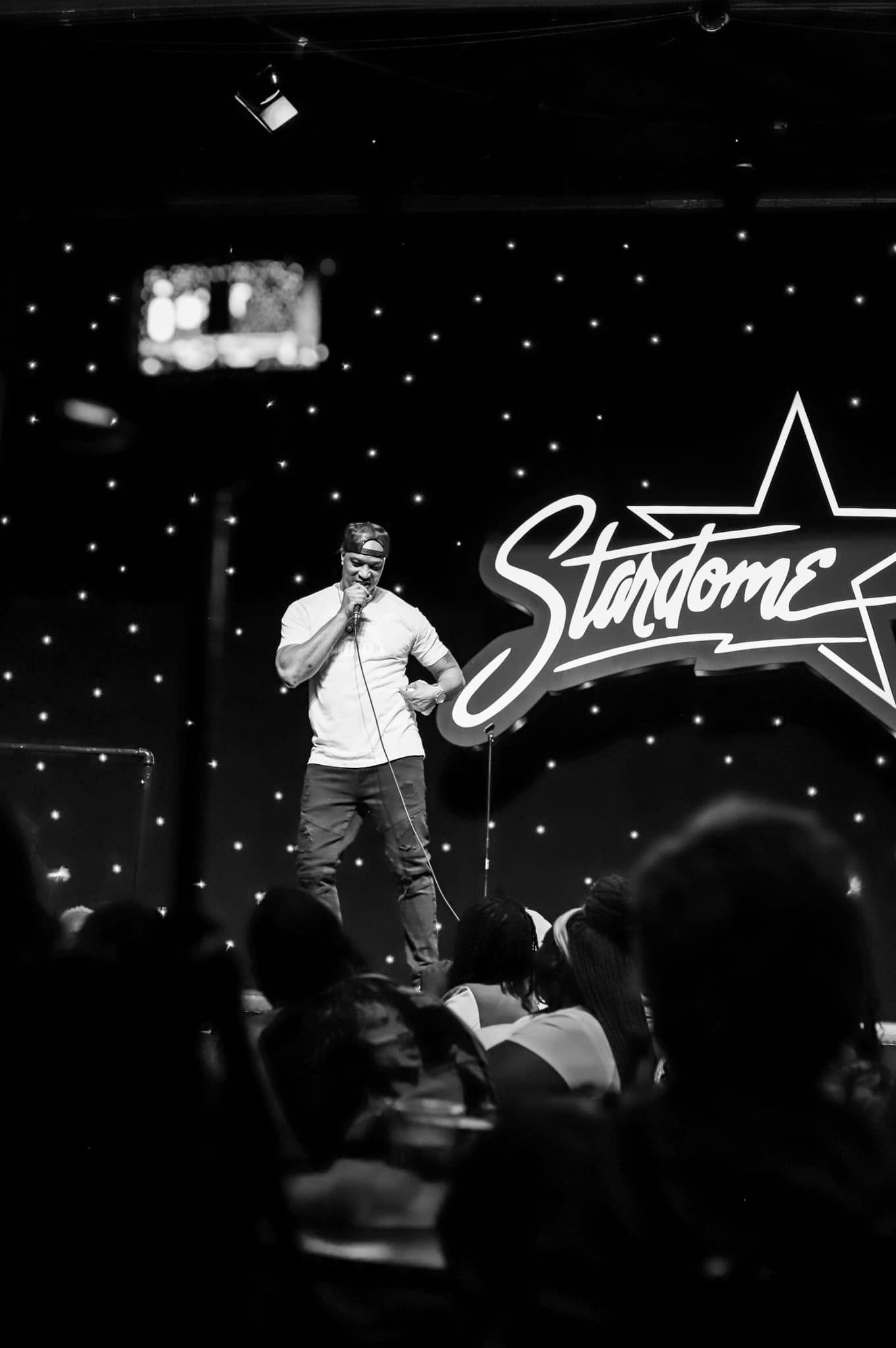 A comedian performs on stage at Stardome comedy club in a black and white photo.