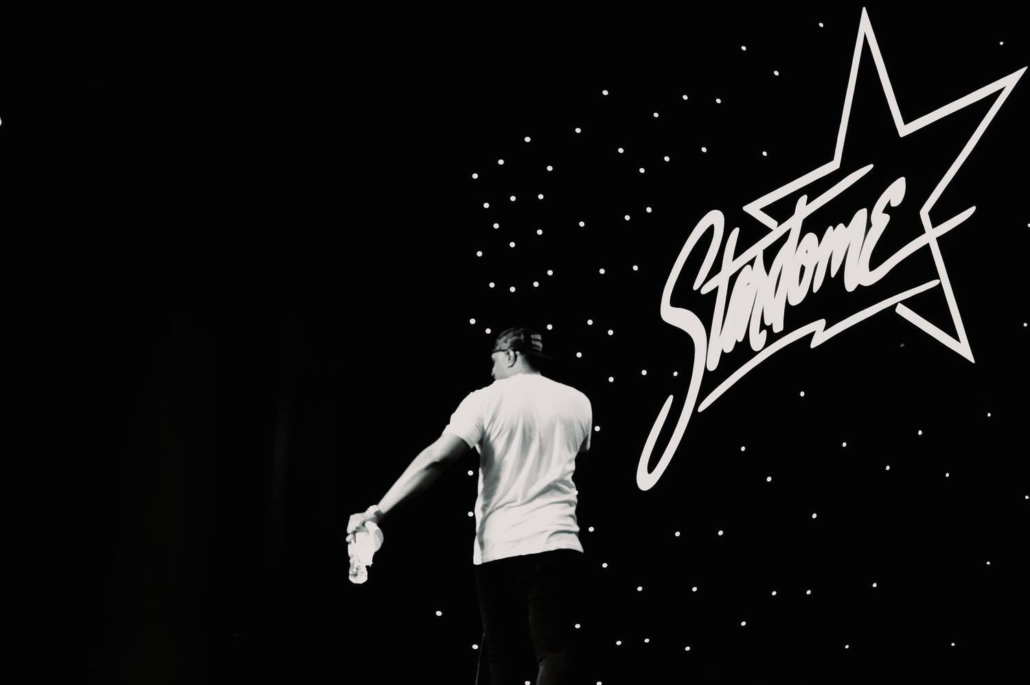 Person on stage facing a glowing Startime sign in a black and white performance photo.