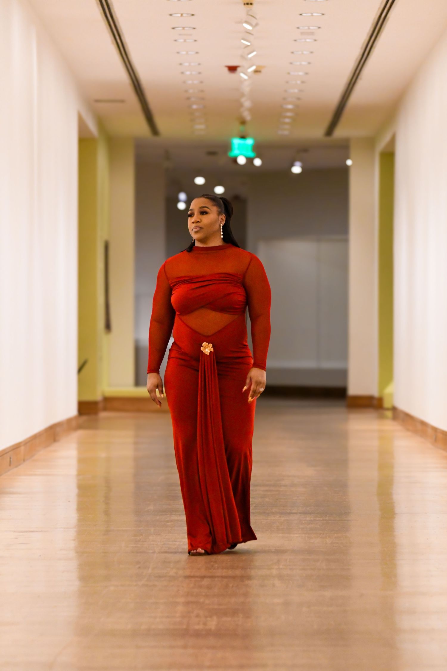 Woman in a stunning red cutout maxi dress walks confidently down a modern hallway.