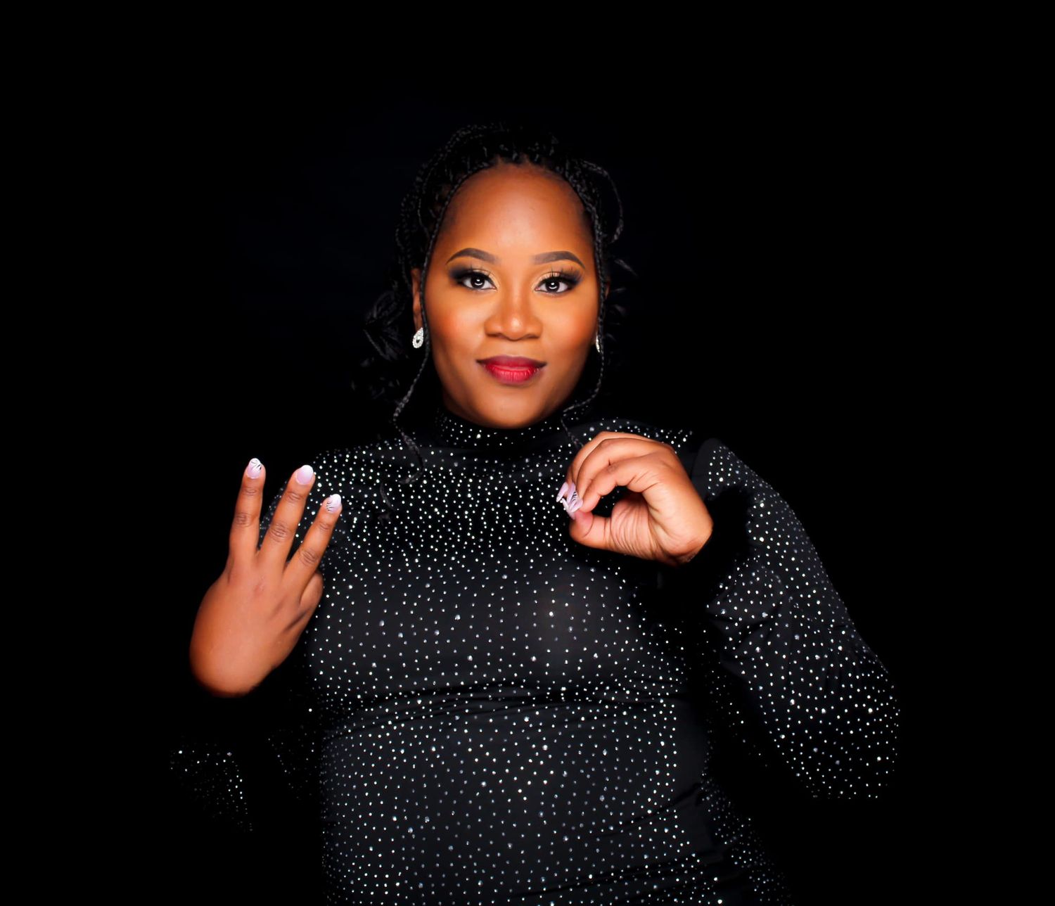 A smiling Black woman in a glittery black dress gestures with her hand against a dark background.