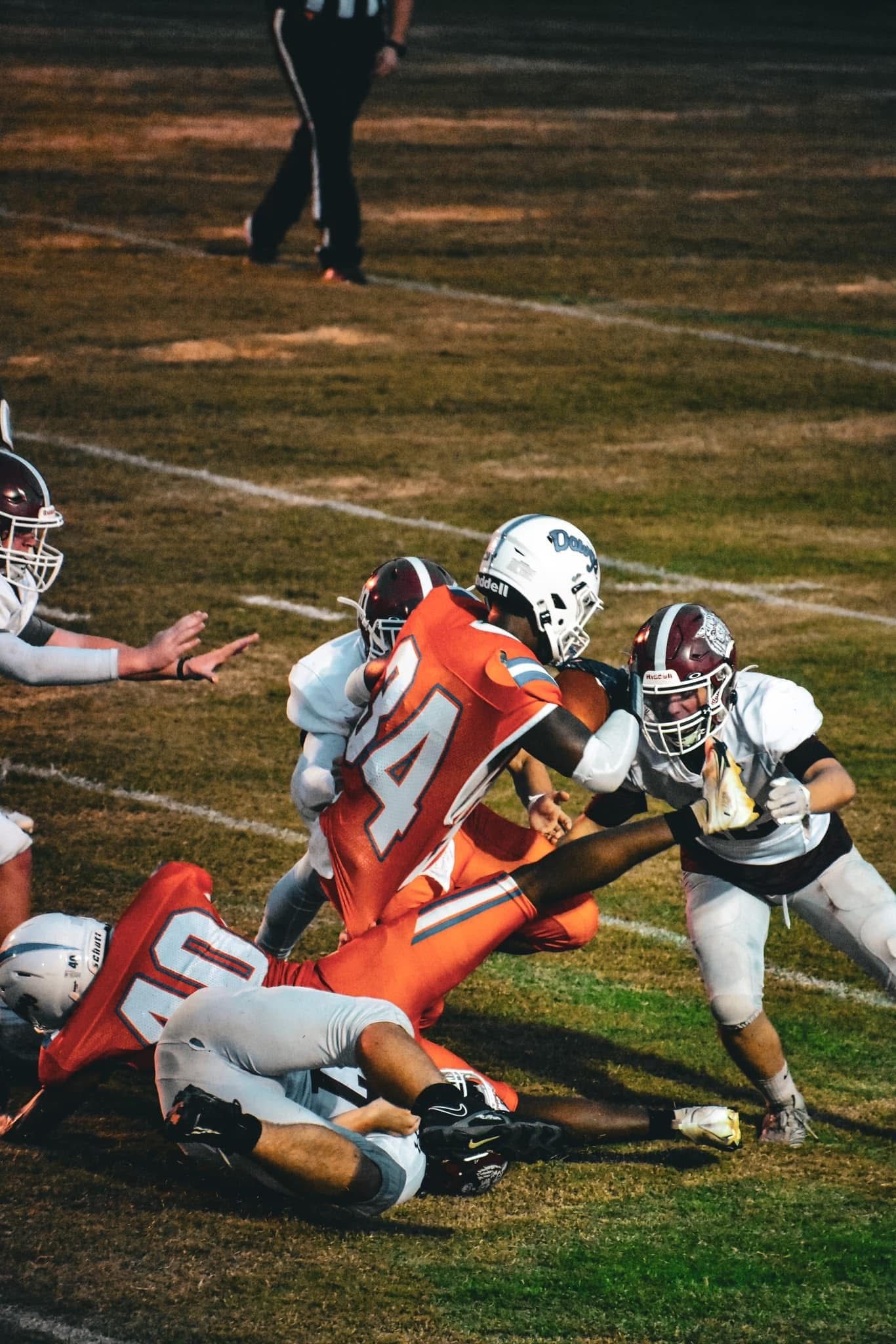 Football players in red and white uniforms collide during an intense night game on a grass field.