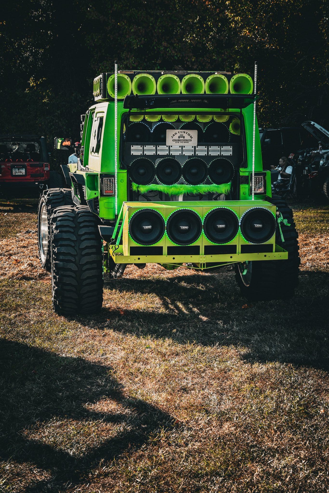 Heavily customized neon green off-road truck with multiple speakers at an outdoor car show.