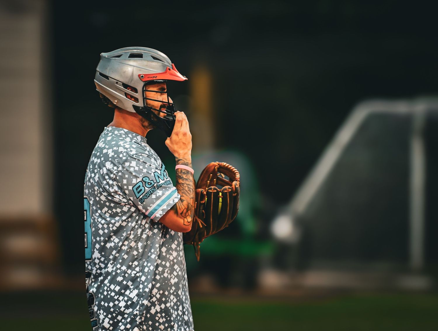 Baseball player in patterned jersey and helmet holds glove on outdoor field during game.