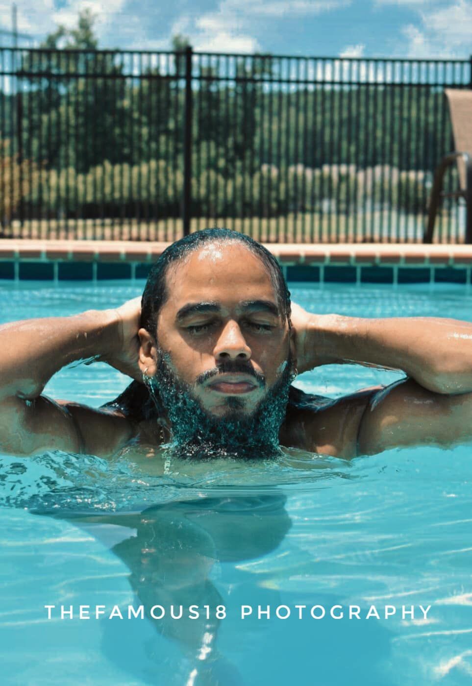 A relaxed man floats peacefully in a swimming pool with his hands behind his head on a sunny day.