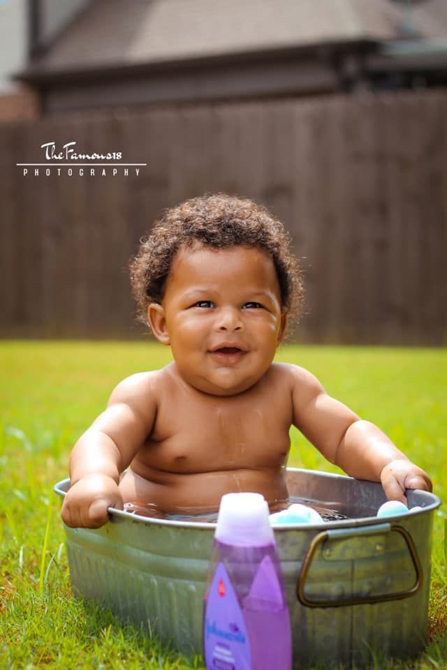 Happy baby smiling while sitting in a metal tub outdoors on green grass with Johnson's baby wash nearby.