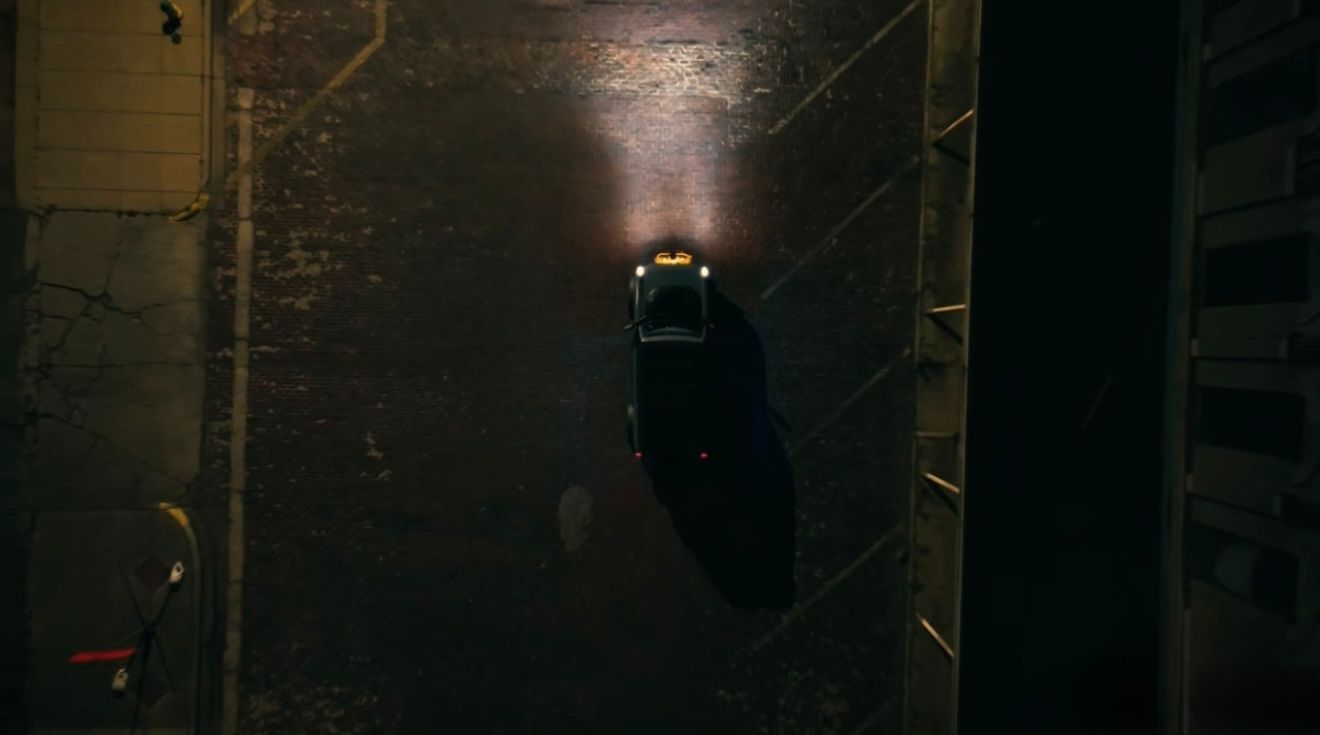 Aerial view of a car driving through a dark narrow alley at night, illuminated by headlights on wet pavement.