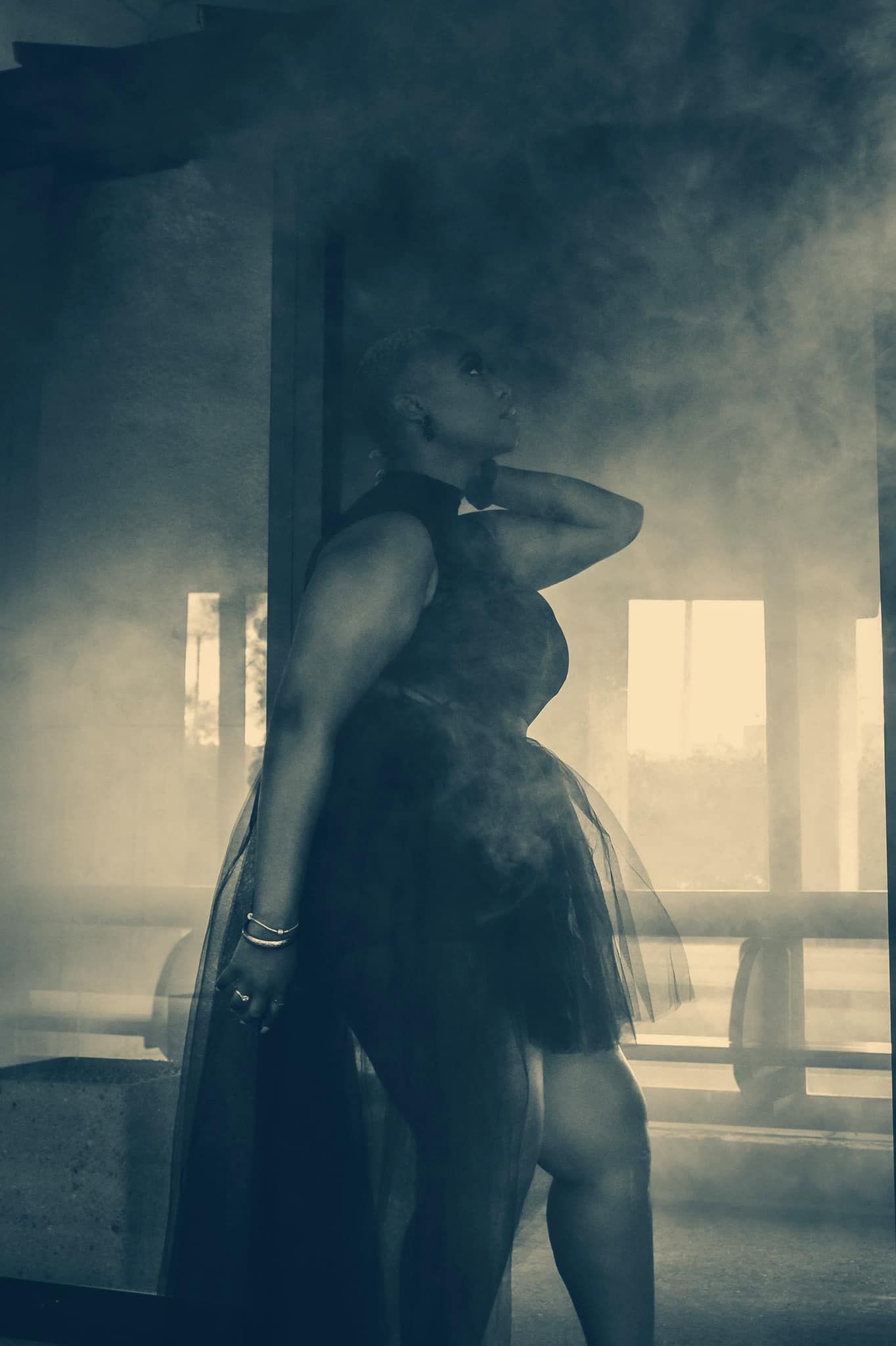 Dramatic silhouette of a woman in a tulle skirt posing in a smoky, moody industrial space.