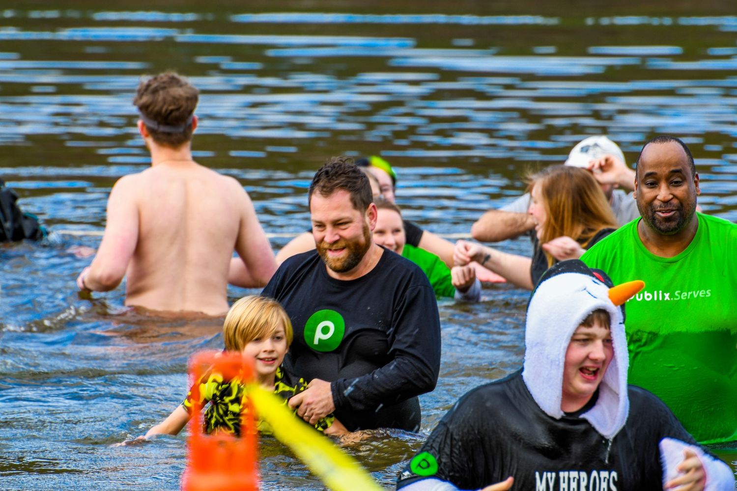 A group of people smiling and wading in a cold river during a charity polar plunge fundraising event.
