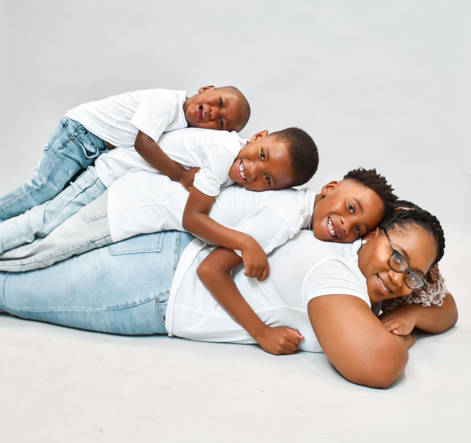 Mother and two young sons pose together lying down in matching white outfits.