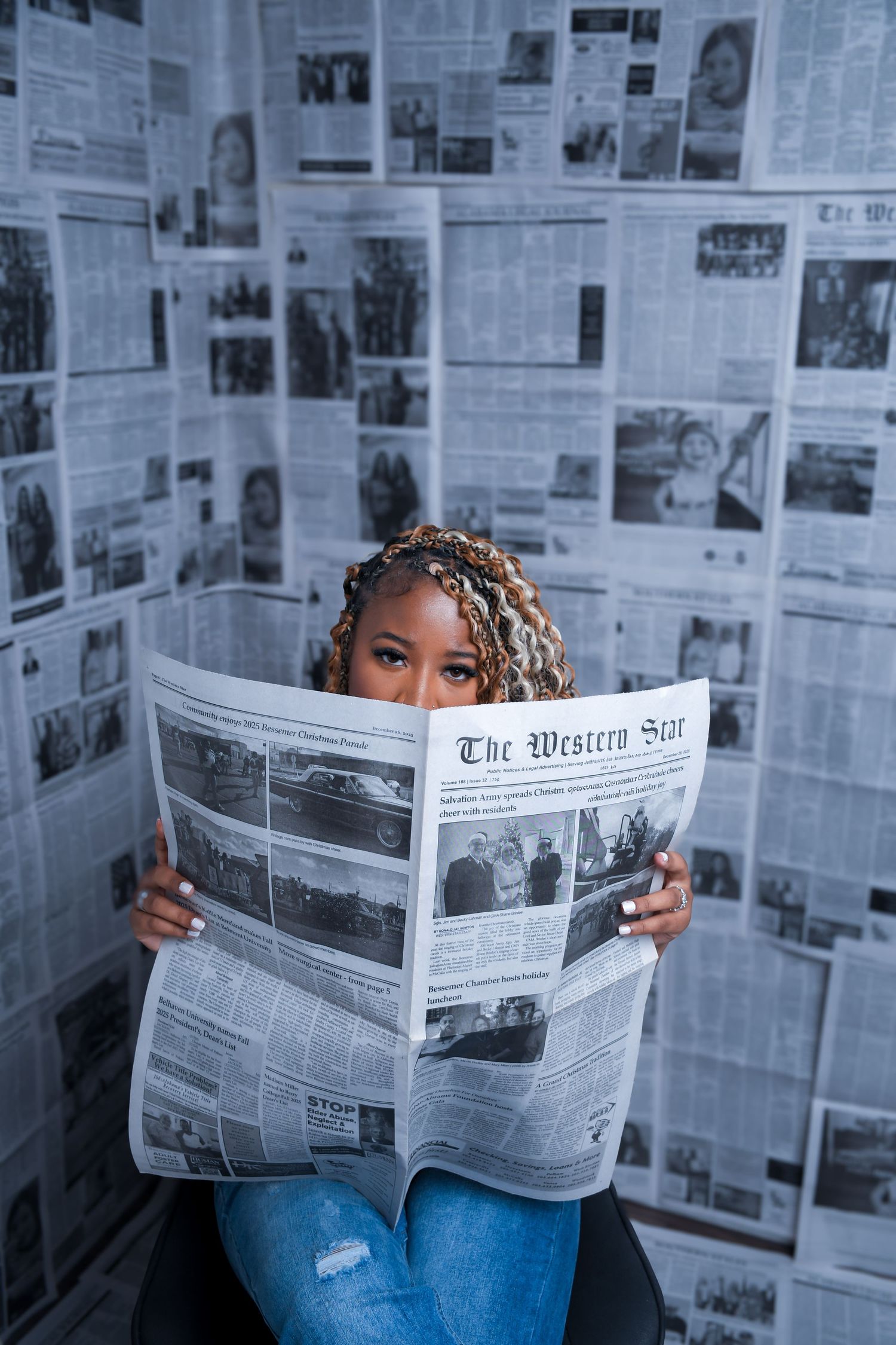 Woman reading The Western Star newspaper against a wall covered in newspaper pages.