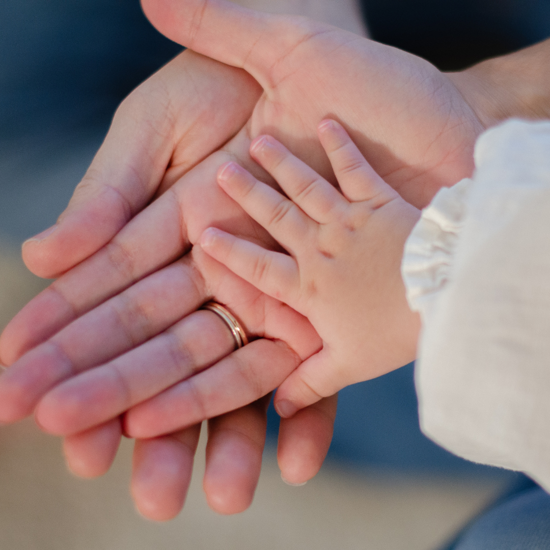 Three generations of hands stacked together, with wedding rings visible, symbolizing family love and unity.