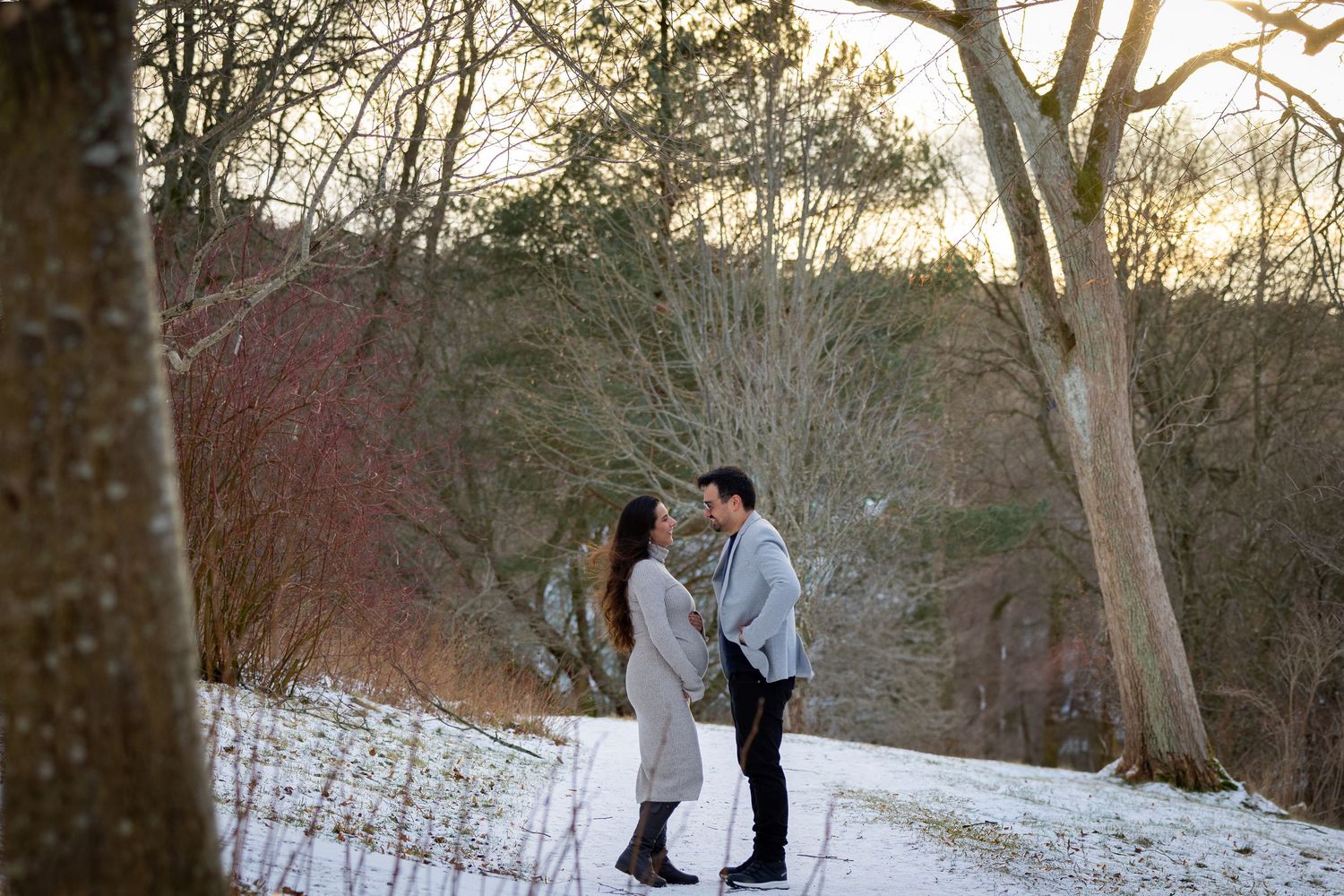 Couple embracing romantically on a snowy forest path during winter maternity session.