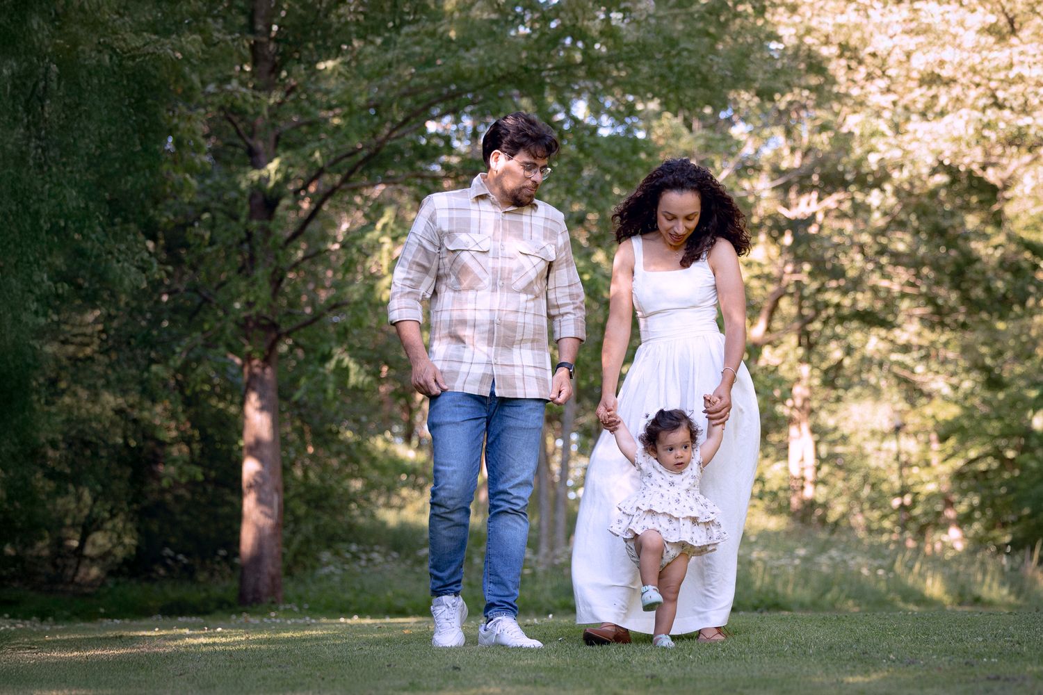 Happy family with mother, father, and toddler daughter walking together in a green park.