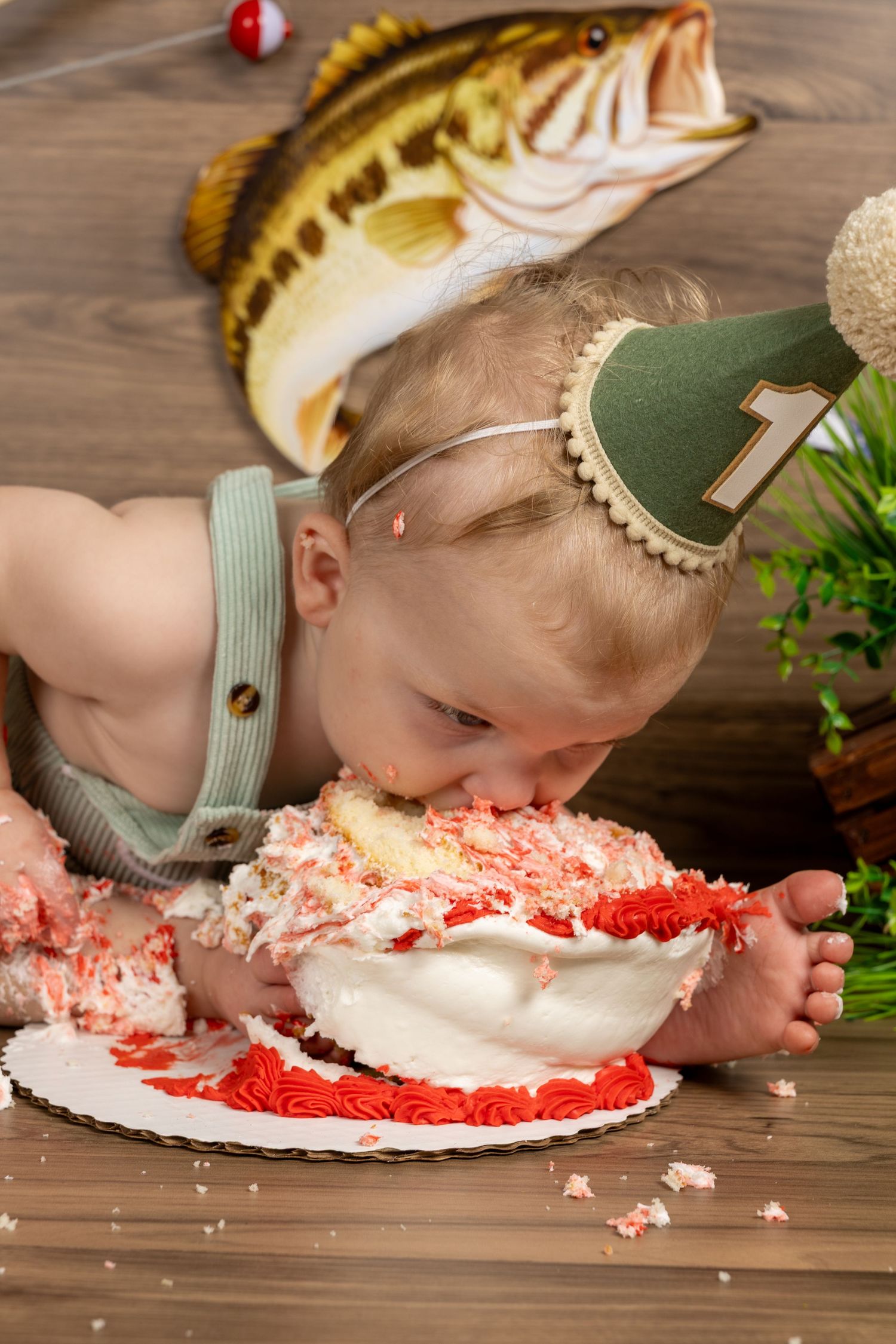 Baby smashing face into first birthday cake with red and white frosting, wearing a number 1 party hat.