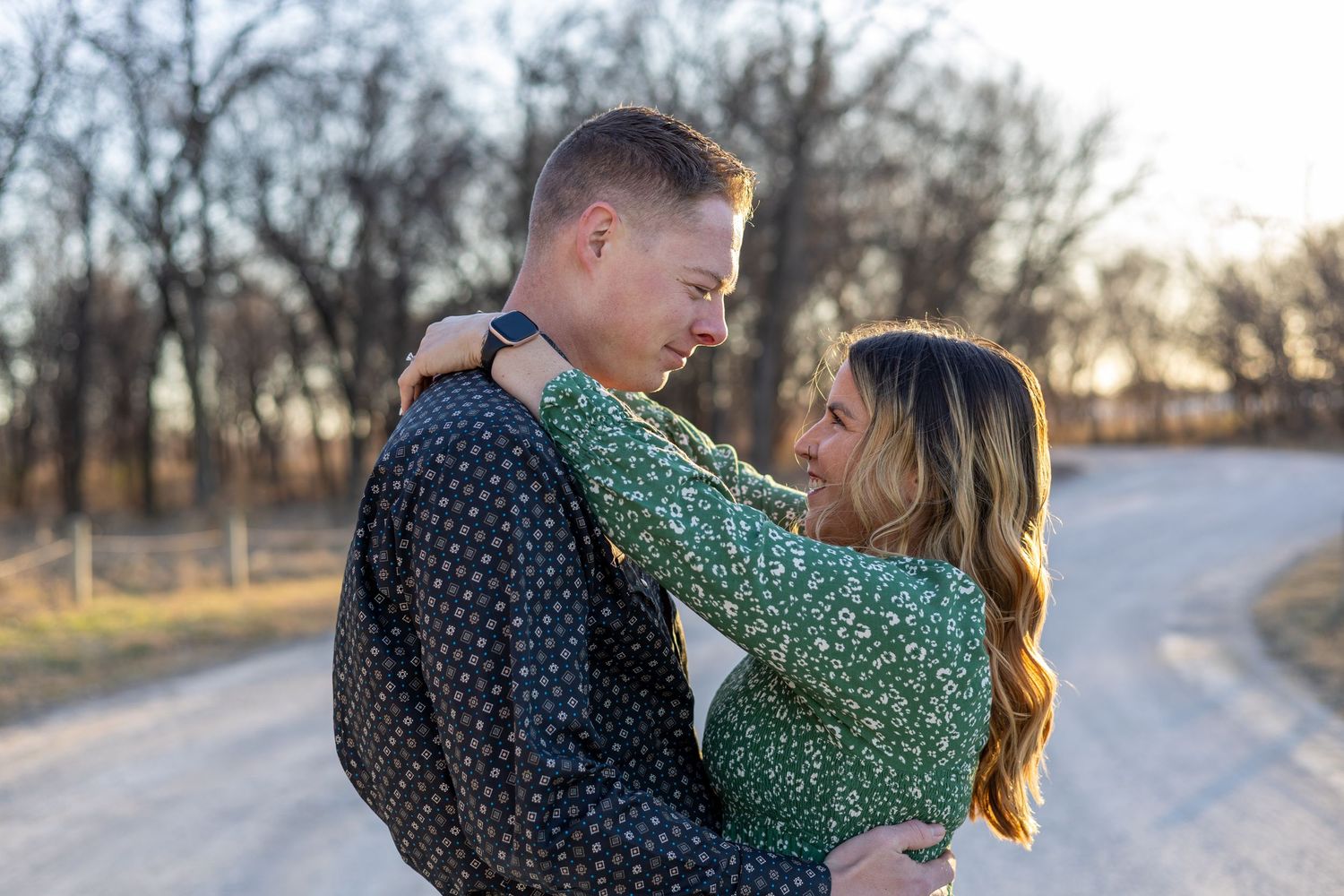 A couple shares an intimate embrace on a tree-lined path during sunset in autumn.