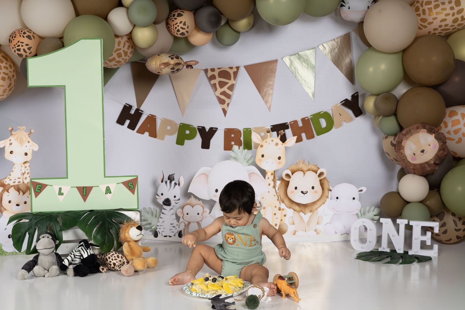 Baby's first birthday cake smash with safari theme, jungle animals, balloon arch, and Happy Birthday banner.