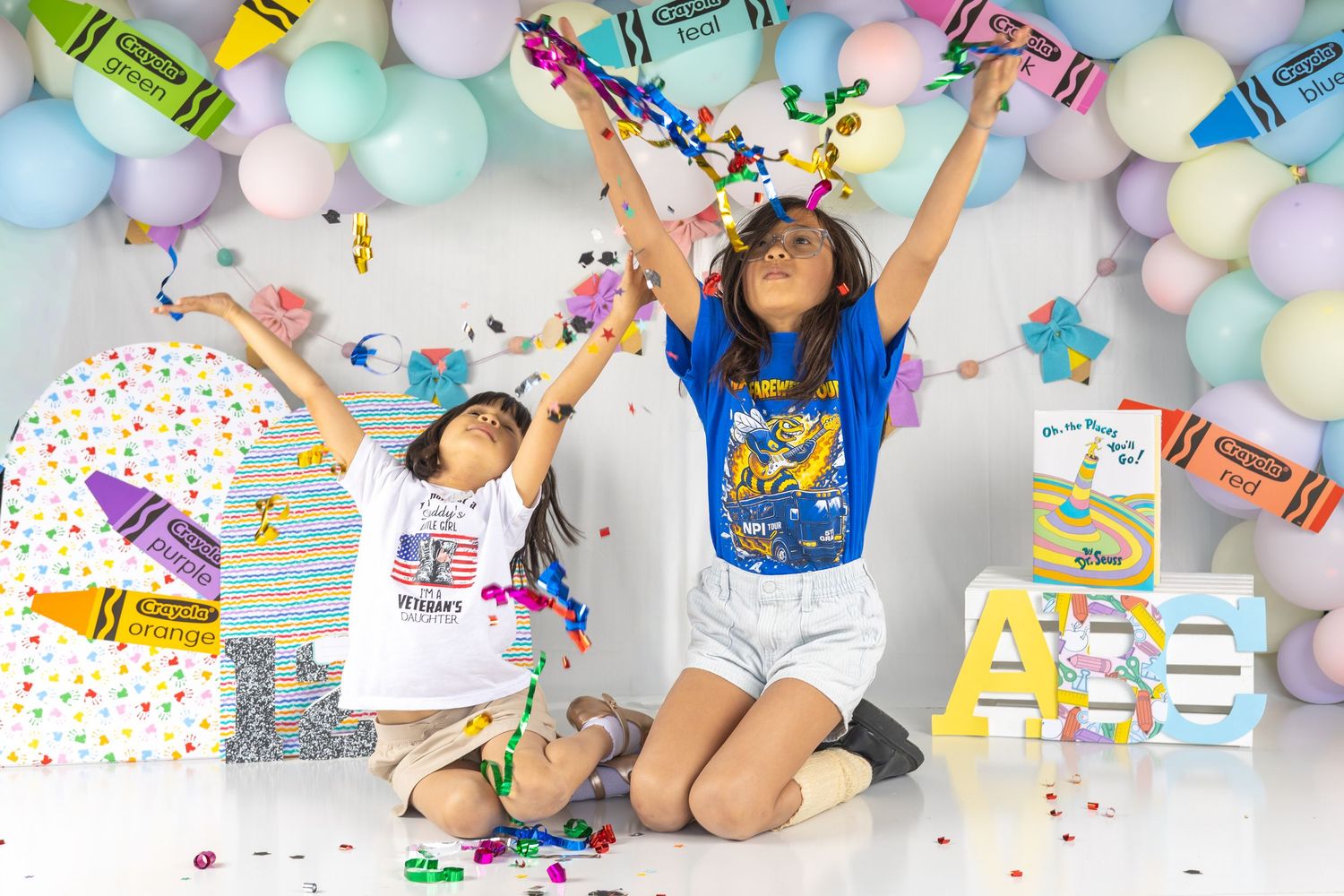 Two kids tossing colorful confetti surrounded by balloons, crayons, and festive decorations at a birthday celebration.