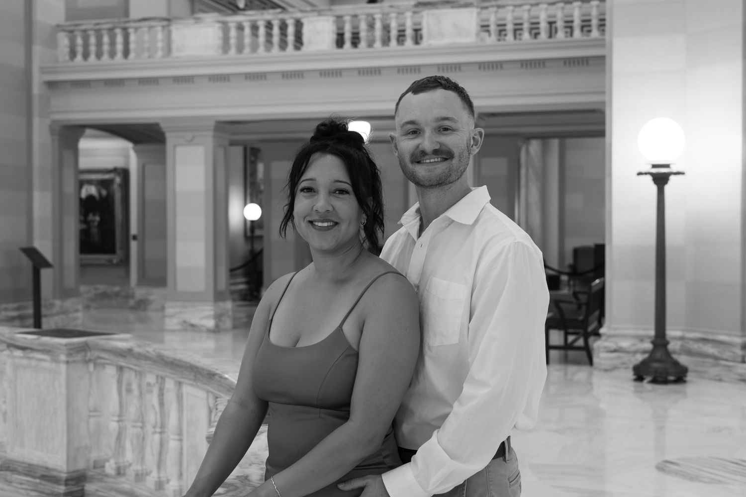 Black and white photo of a smiling couple posing together in an elegant marble building interior.