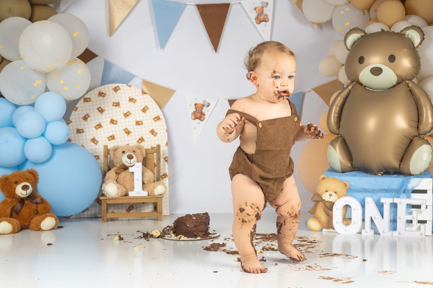 Baby's first birthday cake smash with teddy bear theme, blue and brown balloons, and ONE sign decoration.