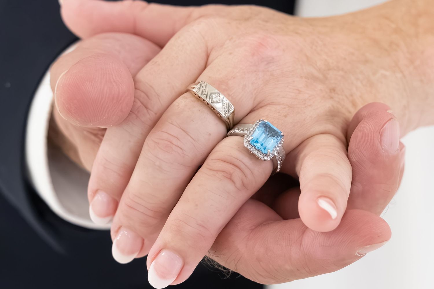 Close-up of two hands wearing elegant silver rings, one featuring a blue topaz gemstone, symbolizing a wedding or engagement.