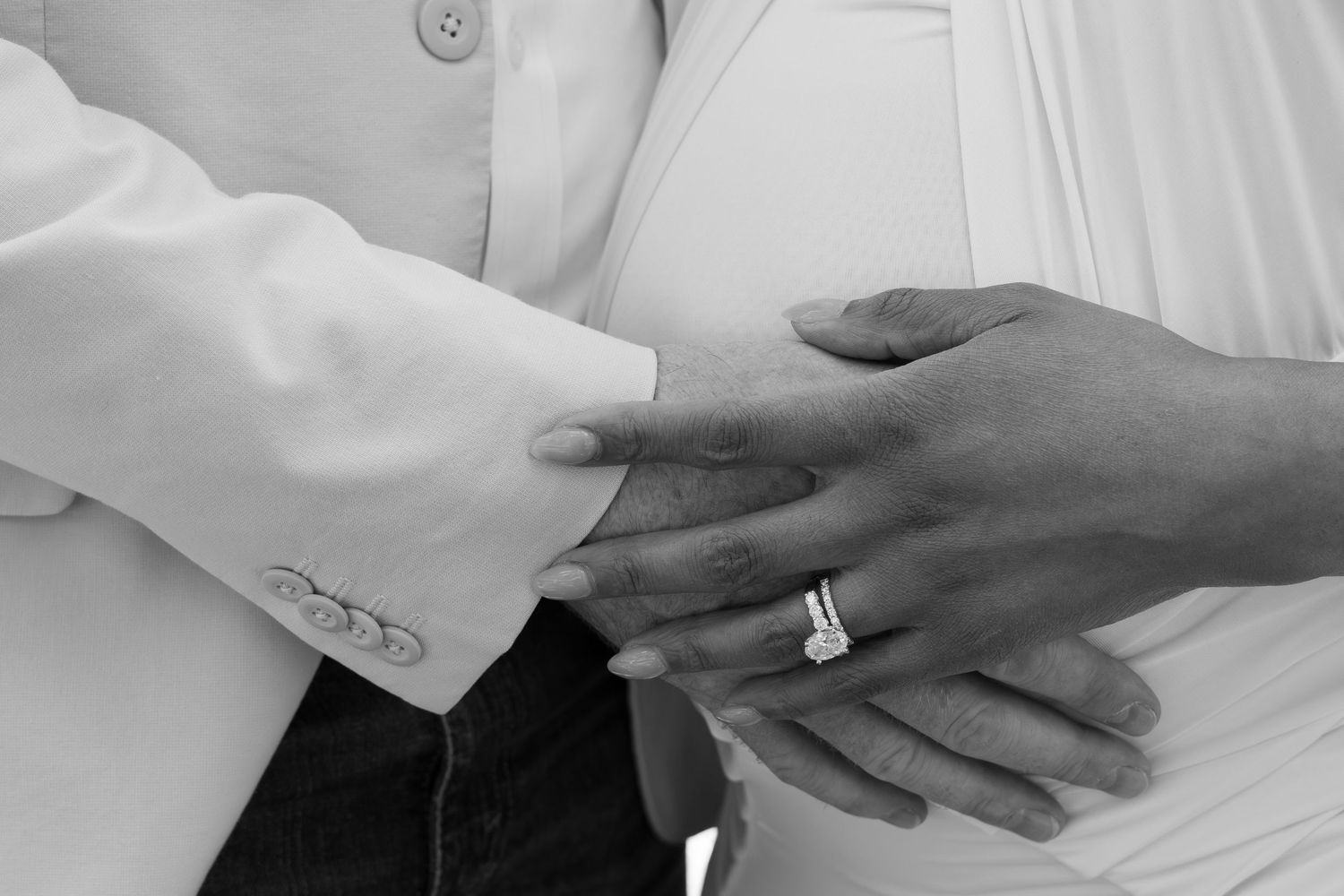Black and white photo of couple holding hands showing diamond engagement and wedding rings.