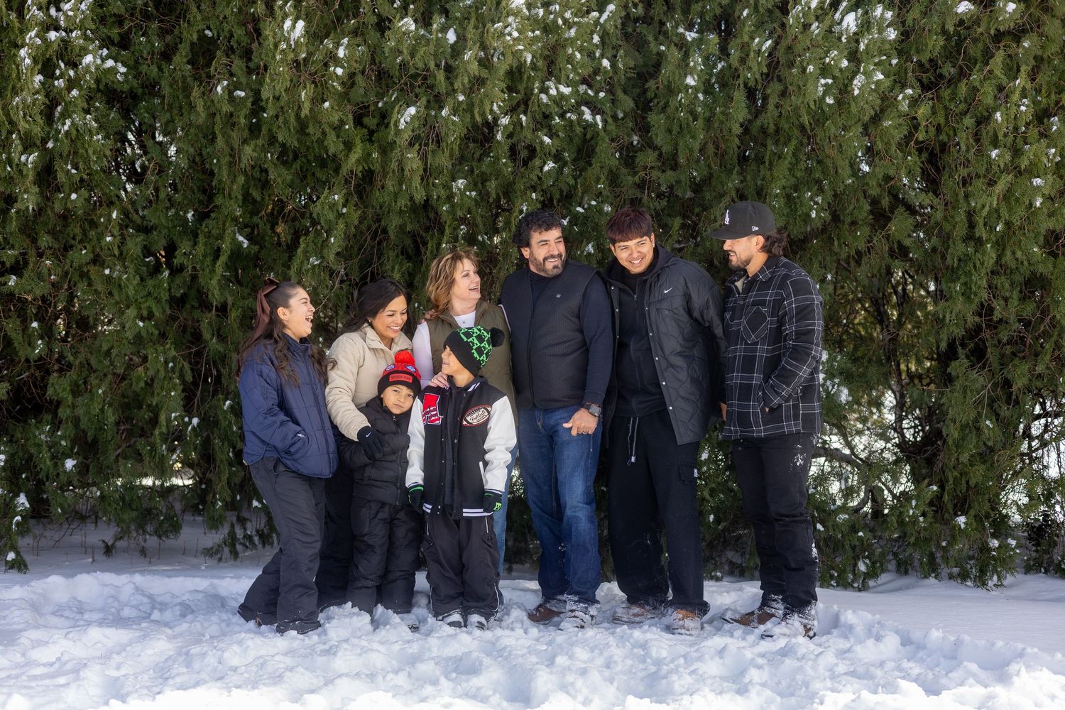 A group of people stand together in front of snow-covered evergreen trees in winter.